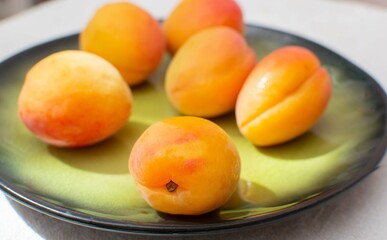 Ripe yellow apricots on a green ceramic plate close-up.