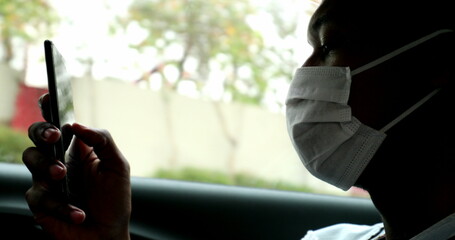 Black African man looking at cellphone inside car wearing surgical mask