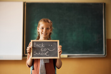 Happy girl holding back to school sign in classroom.