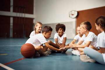 Multiracial group of happy classmates joining hands in unity during PE class at school gym.