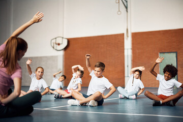 Elementary school children exercising with PE teacher at school gym. © Drazen