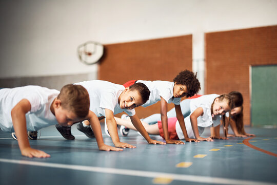 Happy school kids exercising push ups on physical education class at school gym - Powered by Adobe