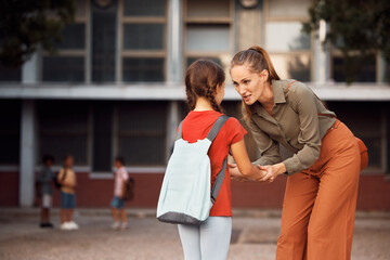 Caring mother talks to her small daughter while saying goodbye  in schoolyard.