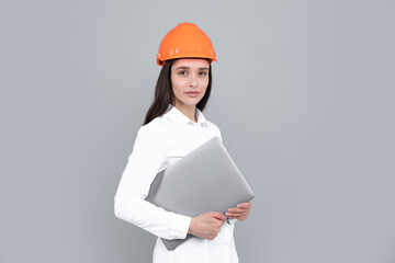 Young woman in hard hat helmet with laptop computer isolated on grey background. Architect woman wear helmet and shirt. Business woman, construction manager, builder.