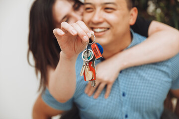 A happy married couple celebrates moving to a new house, shows the keys, stands in an apartment, the concept of a mortgage on real estate.keys close-up