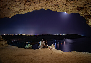 young couple have a romantic night, sitting in the  Calypso cave ,admiring the view of Ramla Bay...