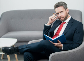 busy mature businessman in suit sit in office making notes in notebook