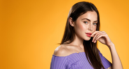 Fototapeta premium Young beauty model, smiling and looking thoughtful at camera, posing against orange background with space for promo text banner