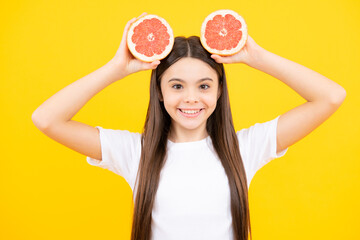 Teenage girl holding a grapefruit on a yellow background. Happy teenager portrait. Smiling girl.