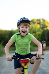 Obraz premium Close-up of a laughing teenager boy in helmet and green T-shirt looking at camera riding a bicycle on the road in the countryside in summer