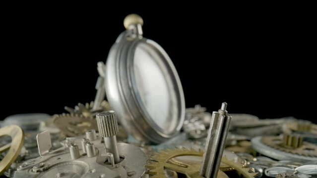 Silver vintage pocket watch dial on pile of clockwork parts. Round old clock among metal gears and cogwheels. Disassembled watch details and vintage pocket watch rotating on black background. Close up