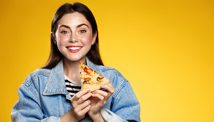 Pizza and delivery concept. Happy woman posing with pizza slice, eating at restaurant, order food take out, orange background