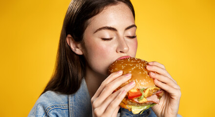 Girl bites cheeseburger with pleasure. Woman eating hambuger, order burger for takeaway food delivery at fastfood restaurant