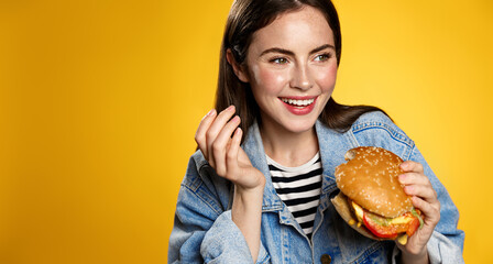 Young woman smiling, casually eating delicious burger. Girl bites hamburger at fast food...