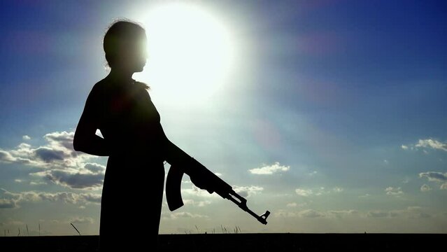 Ukraine War. A young woman with a Kalashnikov assault rifle is training in the field. Silhouette of a girl with a Kalashnikov assault rifle. The concept of war, terrorism, aggression against Ukraine.