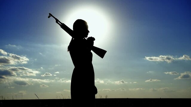 Ukraine War. A young woman with a Kalashnikov assault rifle is training in the field. Silhouette of a girl with a Kalashnikov assault rifle. The concept of war, terrorism, aggression against Ukraine.