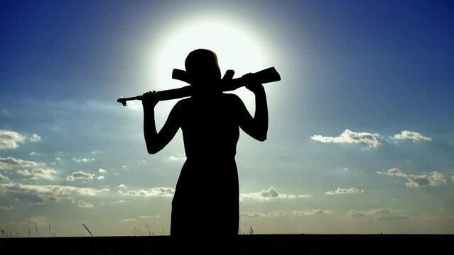 Ukraine War. A young woman with a Kalashnikov assault rifle is training in the field. Silhouette of a girl with a Kalashnikov assault rifle. The concept of war, terrorism, aggression against Ukraine.