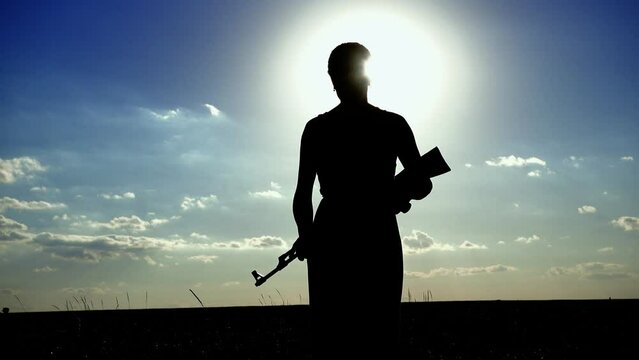 Ukraine War. A young woman with a Kalashnikov assault rifle is training in the field. Silhouette of a girl with a Kalashnikov assault rifle. The concept of war, terrorism, aggression against Ukraine.