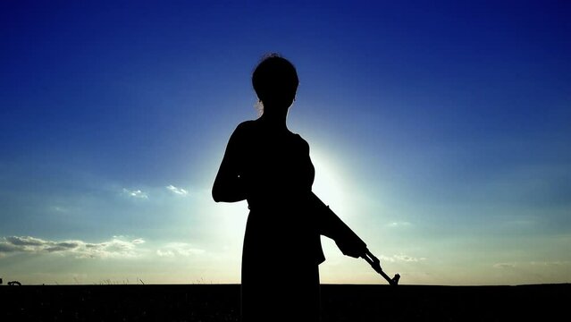 Ukraine War. A young woman with a Kalashnikov assault rifle is training in the field. Silhouette of a girl with a Kalashnikov assault rifle. The concept of war, terrorism, aggression against Ukraine.