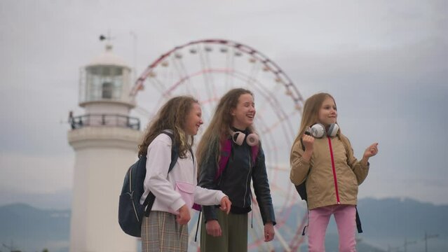 Three laughing school girl friends jump in dance and fool around near Luna park