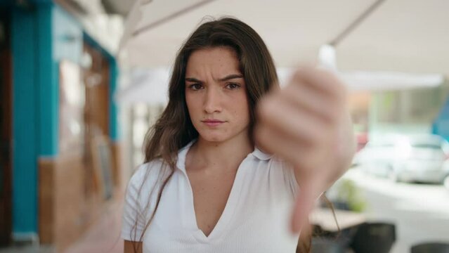 Young hispanic woman doing negative gesture with thumbs down at street