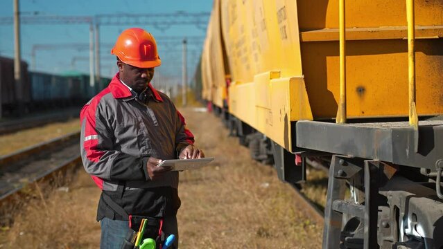 Inspector of wagons at freight train station makes notes in his Tablet PC. African american railroadman with tablet computer at freight train terminal