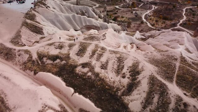 Aerial top view of unique valleys with limestone hills and walking tourists filmed by drone. Natural heritage of uchisar cave town with unusual mountains and rocks. Visiting popular travel destination