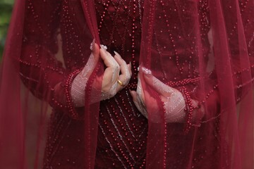 Closeup of a female in a red dress holding a vail with her white henna-painted hands