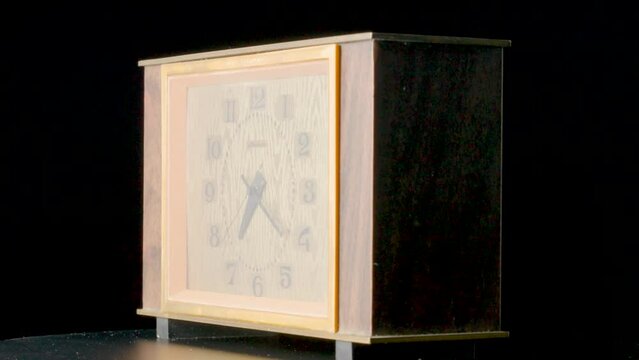 Old wooden clock with ticking hands. Brown vintage timepiece from USSR with wooden case rotating on an isolated black background. View of face and back. Table clock with numbers and spinning hands.