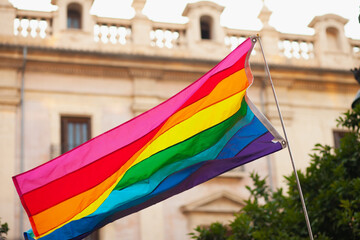 Progressive Pride flag in the air. Rainbow colors flag flaunting in the wind in the streets of Valencia at public pride march event.