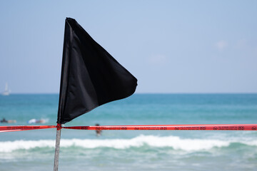 Black flag with a red ribbon on the sea shore warning about dangerous current and waves or invasion...