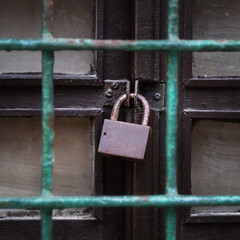 Old padlock on the old wooden door behind a grid