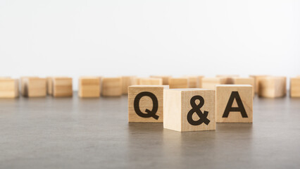 three wooden blocks with letters Q and A with focus to the single cube in the foreground in a conceptual image on grey background