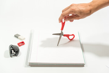 hand using scissors on paper, stapler pencil, sharpener and eraser on the table