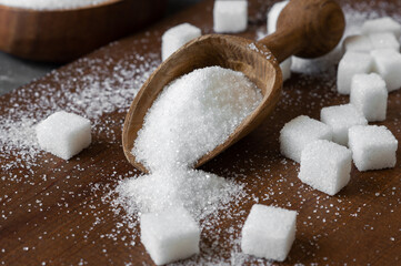 Heap of white granulated sugar in spoon and bowl with sugar cube