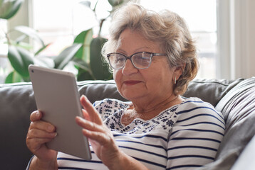 Senior woman sitting on couch at home using wireless tablet