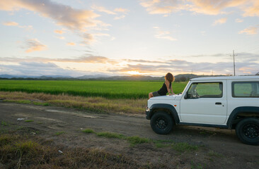 Fototapeta na wymiar girl sitting on the hood of a car watching the sunset
