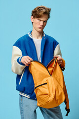 a handsome red-haired guy student stands in a blue bomber jacket with an open orange backpack in...