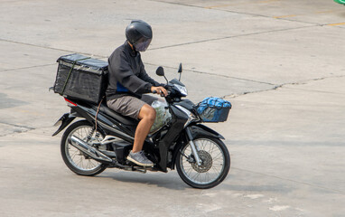 Obraz na płótnie Canvas A man rides a motorcycle with a storage box down the street