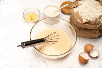 the process of making dough for pancakes with ingredients on a light table, eggs and flour are whipped with a mixer