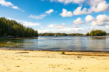 A small yacht at anchor seen from a beach with boreal forest blue sky and white clouds in the...
