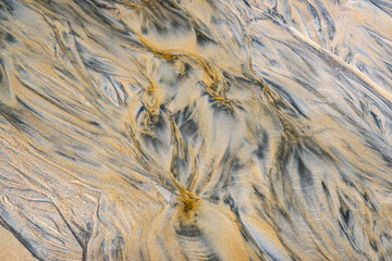 Abstract patterns in beach sand let by the retreating tide.