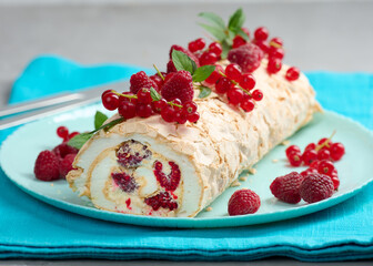 Baked meringue roll with red berries on a round plate, white background