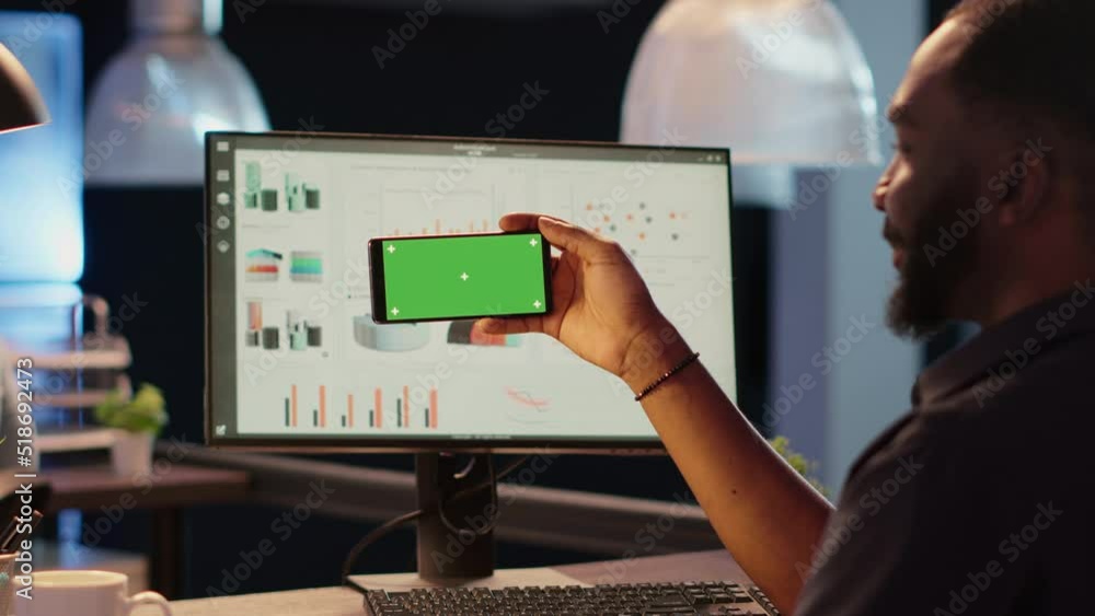 Poster Office worker holding smartphone with horizontal greenscreen in business office late at night. Looking at chromakey background with isolated display and mockup copyspace template.