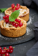 Fruit tart with red currants sprinkled with powdered sugar on a black table, delicious dessert