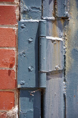 An weathered blue iron door hinge on an old red brick wall building