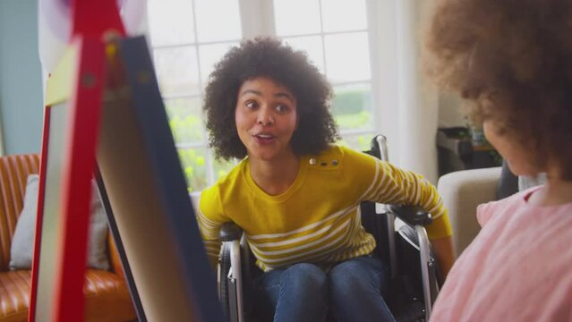 Mother in wheelchair watching daughter having fun drawing picture on whiteboard at home- shot in slow motion