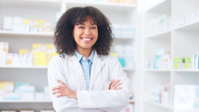 A proud pharmacist standing in front of medicine shelves in a drugstore. Young female healthcare professional standing with her arms crossed, wearing a lab coat and smiling in a pharmacy