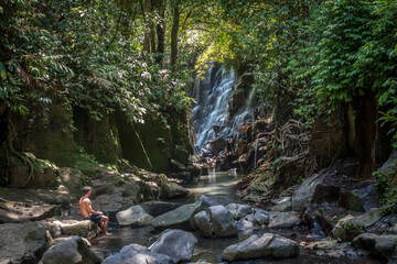 boy watching waterfall sitting in river
