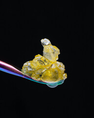 Live resin diamonds sitting on a rainbow-colored titanium dab tool with a black background. 